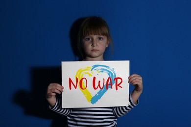 Image of Sad little girl holding paper with phrase No War on blue background