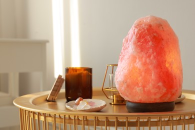 Photo of Himalayan salt lamp, candles and crystals on golden table indoors, space for text