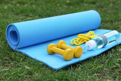 Photo of Skipping rope, dumbbells and bottle of water on fitness mat outdoors. Morning exercise