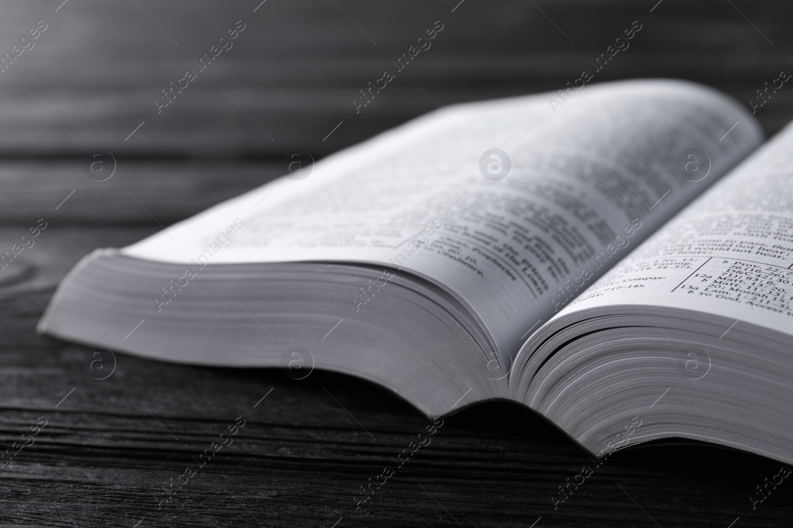 Photo of Open Bible on black wooden table, closeup. Christian religious book