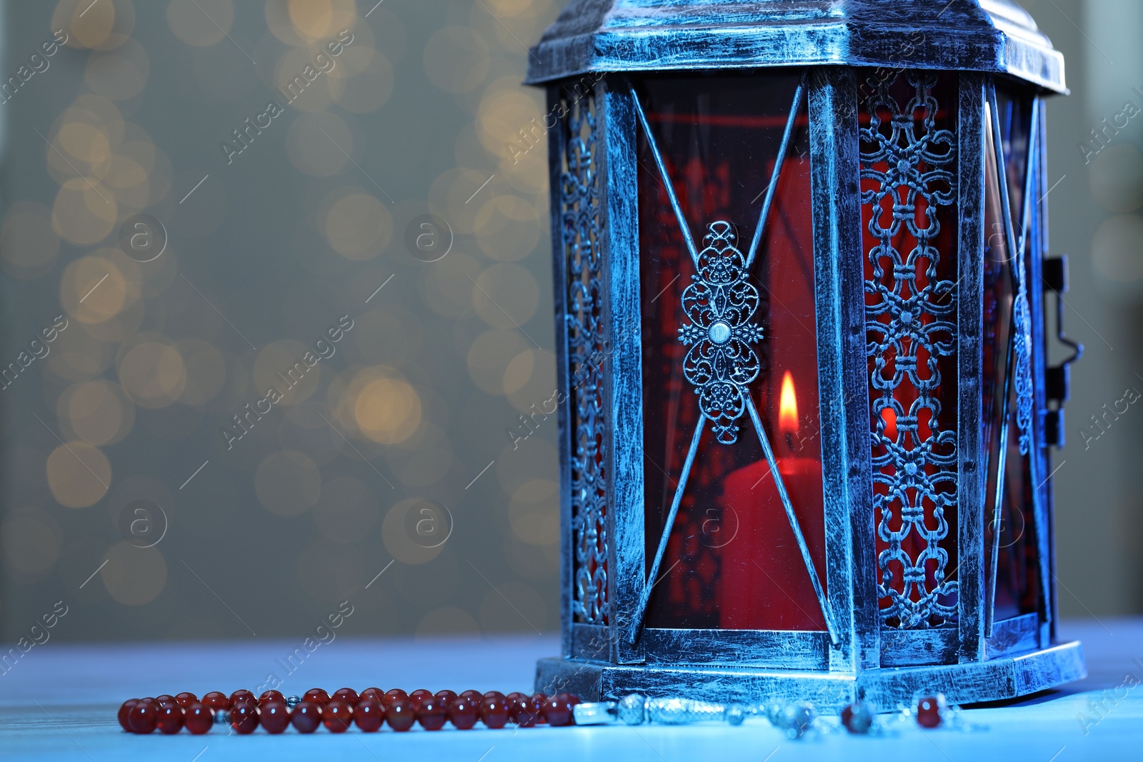 Photo of Arabic lantern and misbaha on table against blurred lights, space for text