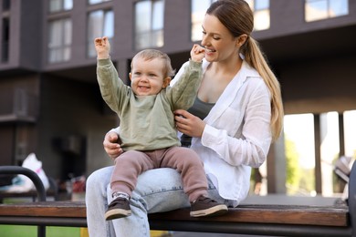 Happy nanny with cute little boy on bench outdoors