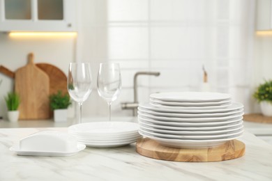 Photo of Clean plates, glasses and butter dish on white marble table in kitchen