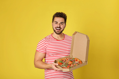 Handsome man with tasty pizza on yellow background