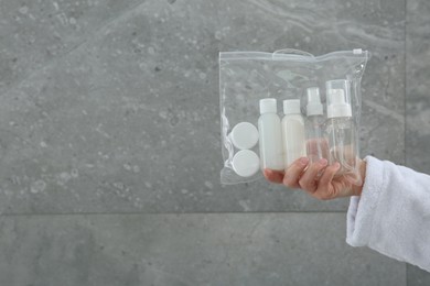 Photo of Woman holding plastic bag of cosmetic travel kit near grey wall, closeup and space for text. Bath accessories