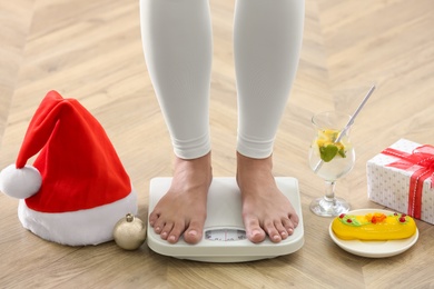 Photo of Woman using scale surrounded by food and alcohol on floor, closeup. Overweight problem after New Year party