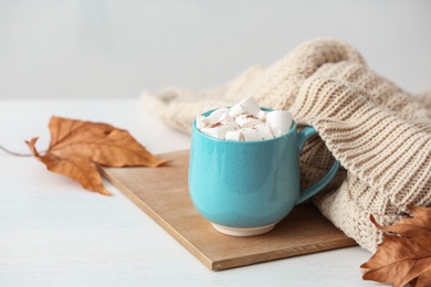 Cup of hot cozy drink with marshmallows and autumn sweater on table. Space for text