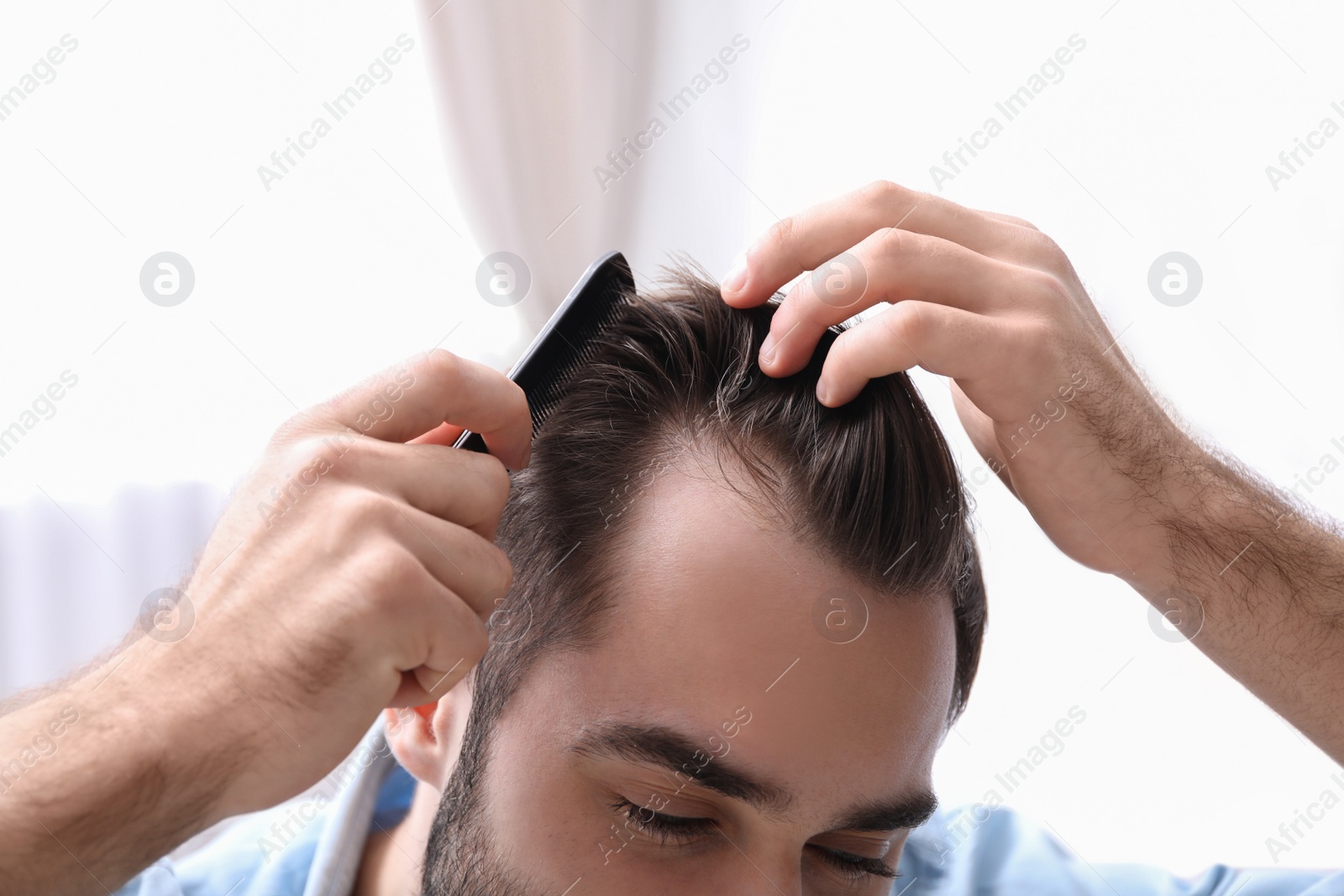 Photo of Young man with comb indoors, closeup. Hair loss problem