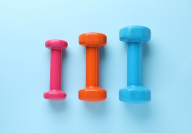 Different stylish dumbbells on light blue background, flat lay
