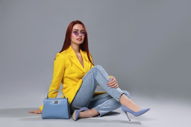 Stylish woman with red dyed hair and bag sitting on light gray background