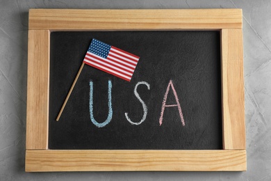 Photo of Chalkboard with written word USA and national flag on grey background, flat lay