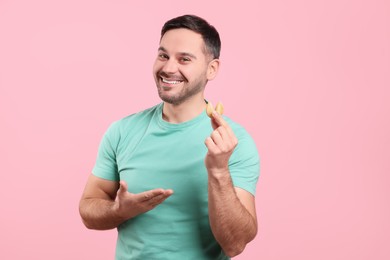 Photo of Happy man holding tasty fortune cookie with prediction on pink background. Space for text