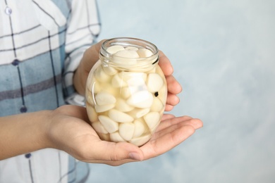 Woman holding jar with pickled garlic on light background, closeup