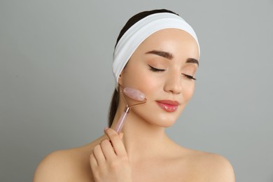 Woman using natural pink quartz face roller on grey background