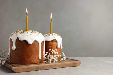 Tasty Easter cakes with burning candles on grey table. Space for text