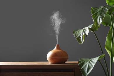 Photo of Air humidifier on chest of drawers near green houseplant against grey wall