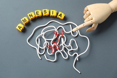 Photo of Word Amnesia, brain made of wires and mannequin hand on grey background, flat lay