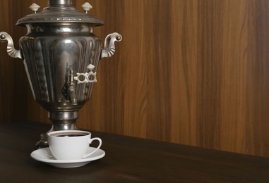 Photo of Vintage samovar and cup of hot drink served on wooden table, space for text. Traditional Russian tea ceremony