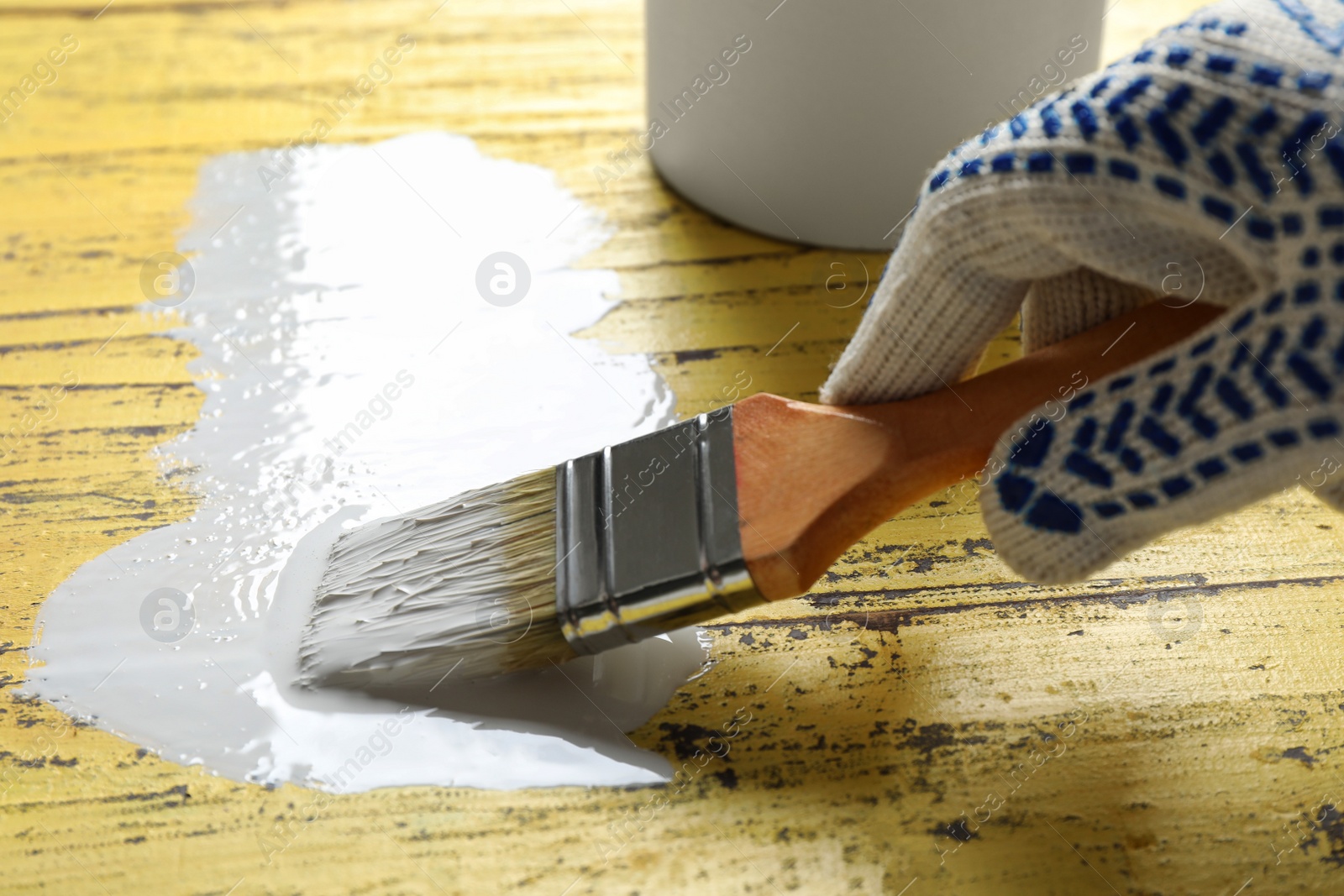 Photo of Person making brush stroke with white paint on yellow wooden table, closeup. Space for text