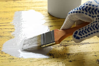 Photo of Person making brush stroke with white paint on yellow wooden table, closeup. Space for text