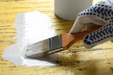 Person making brush stroke with white paint on yellow wooden table, closeup. Space for text