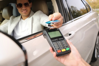 Photo of Man sitting in car and paying with credit card at gas station, focus on hand