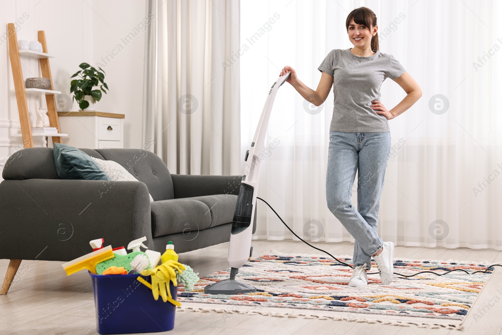 Photo of Happy young housewife vacuuming rug at home