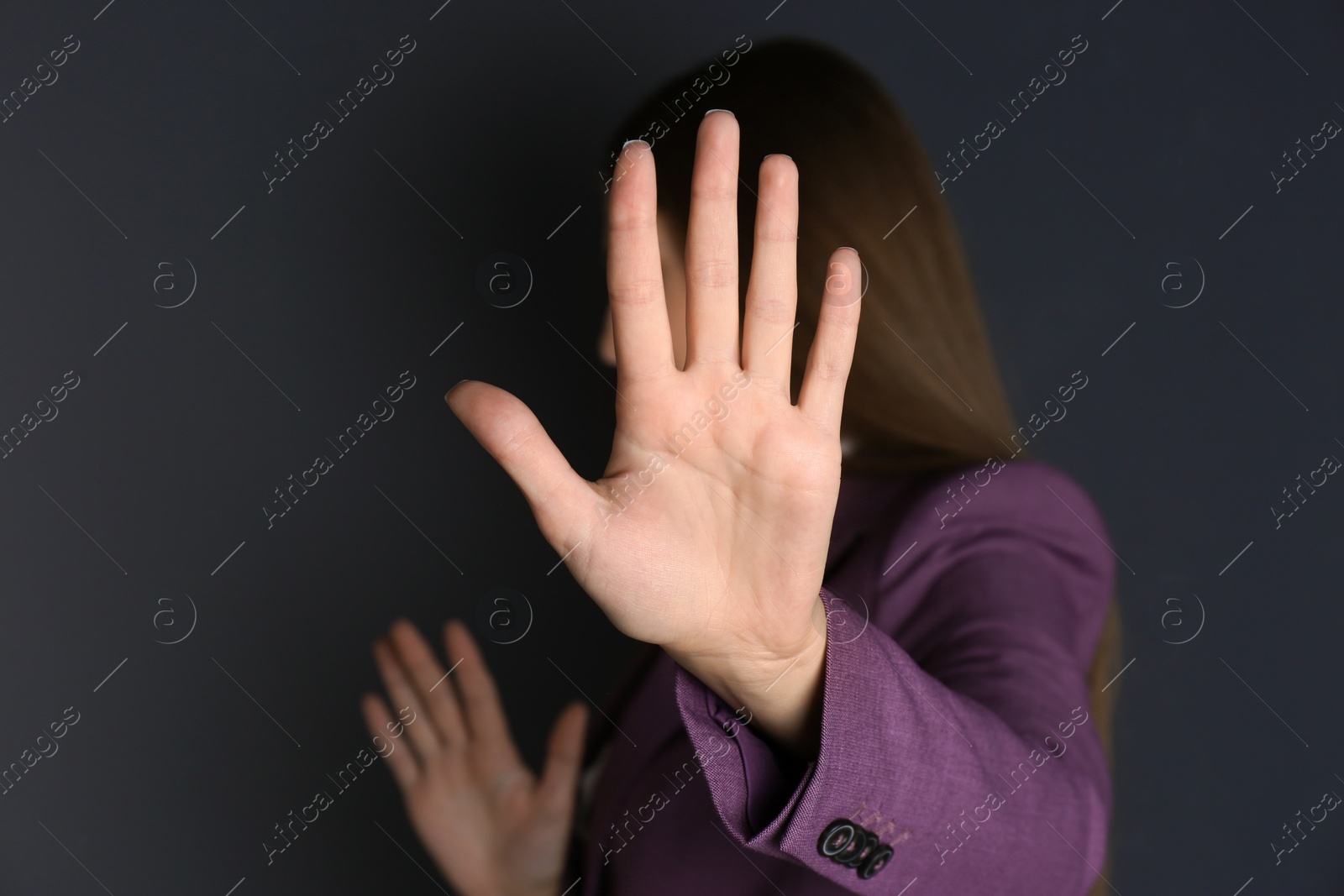 Photo of Woman showing stop gesture on dark background. Problem of sexual harassment at work