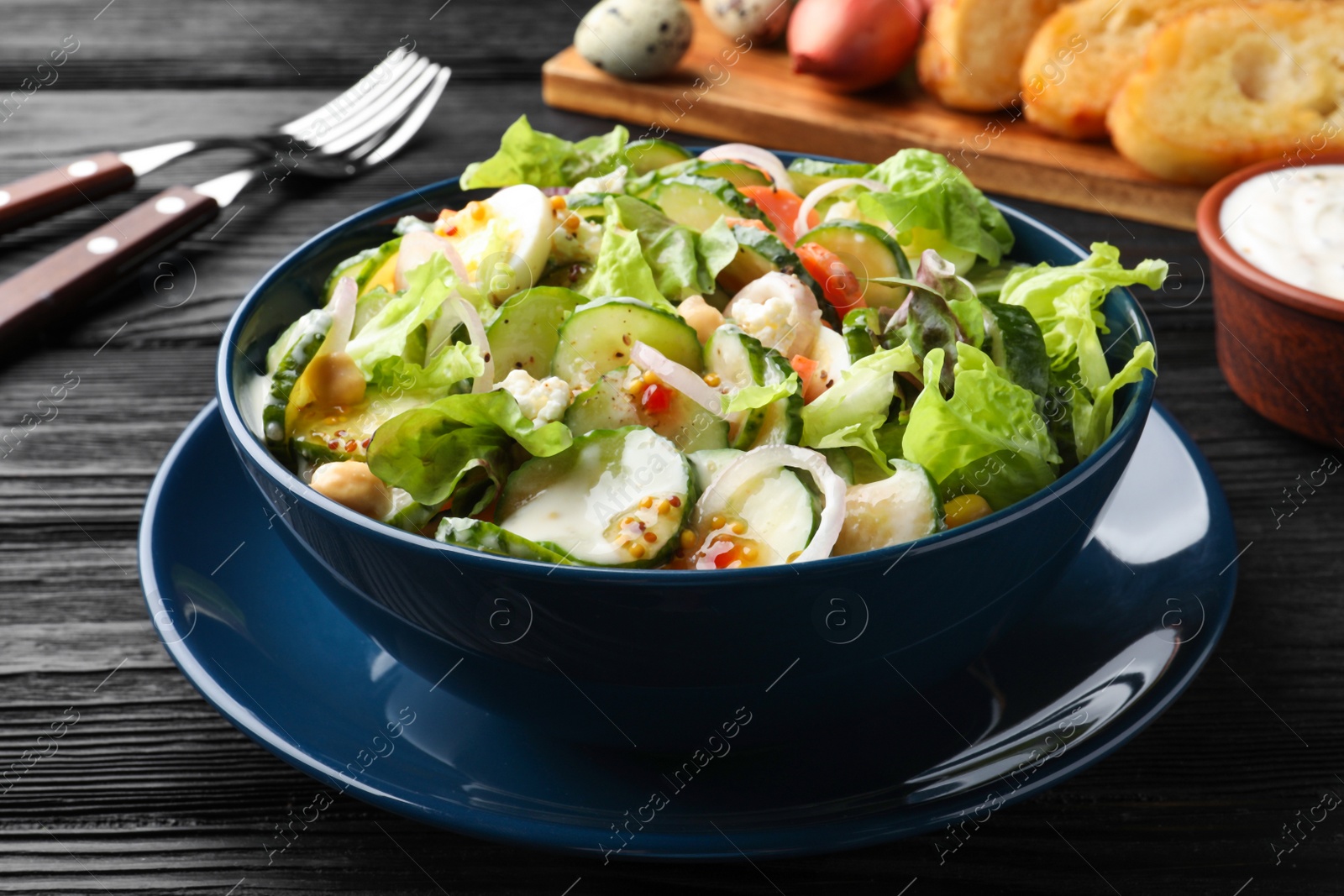 Photo of Bowl of delicious cucumber salad served on black wooden table, closeup