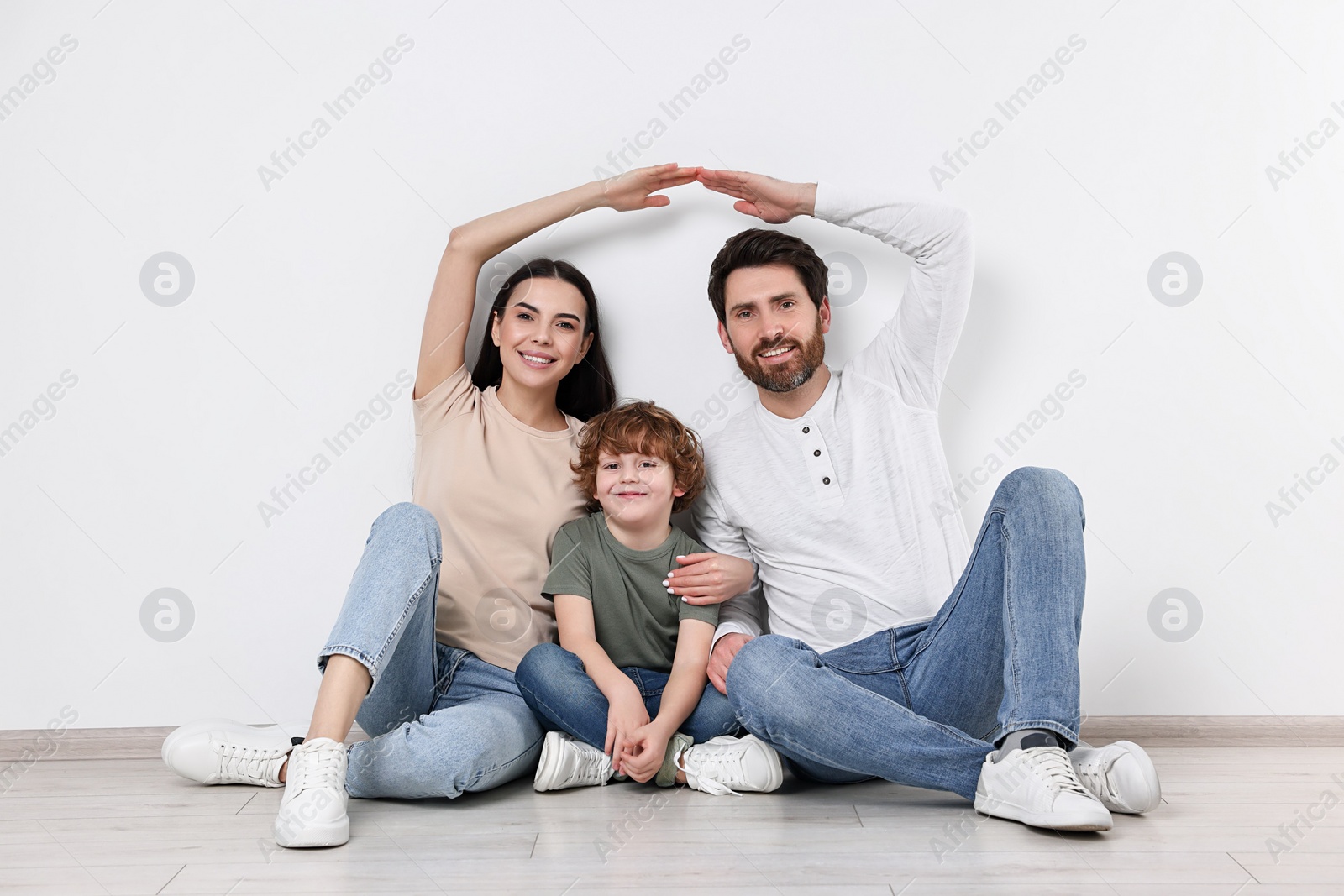 Photo of Family housing concept. Happy woman and her husband forming roof with their hands while sitting with son on floor at home