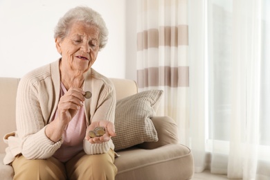 Photo of Elderly woman counting coins in living room. Space for text