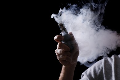 Photo of Man using electronic cigarette on black background, closeup. Space for text