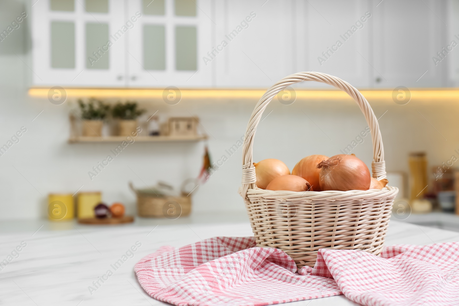 Photo of Fresh onions on white table in modern kitchen. Space for text