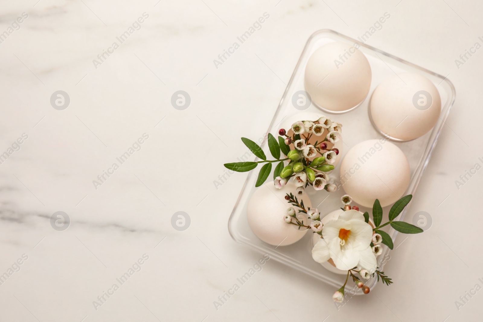 Photo of Easter eggs and beautiful flowers on white marble table, top view. Space for text