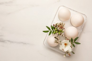 Easter eggs and beautiful flowers on white marble table, top view. Space for text