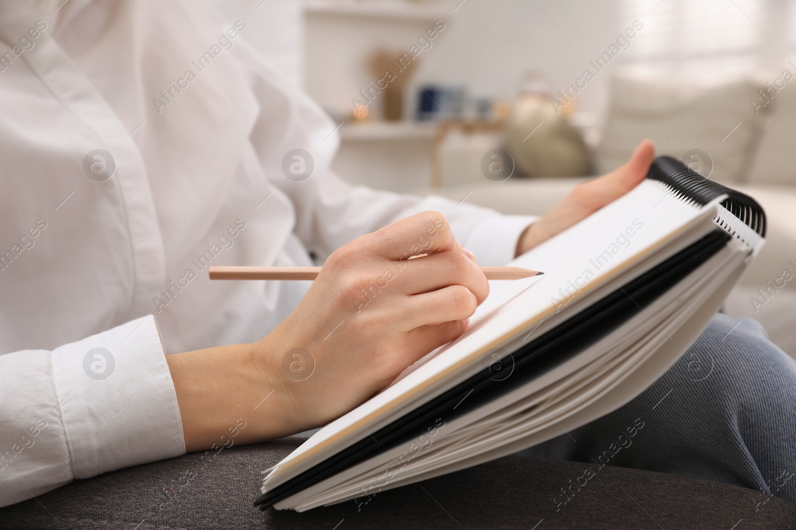 Photo of Woman drawing in sketchbook with pencil at home, closeup