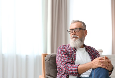 Photo of Portrait of handsome mature man with glasses sitting on chair in room. Space for text