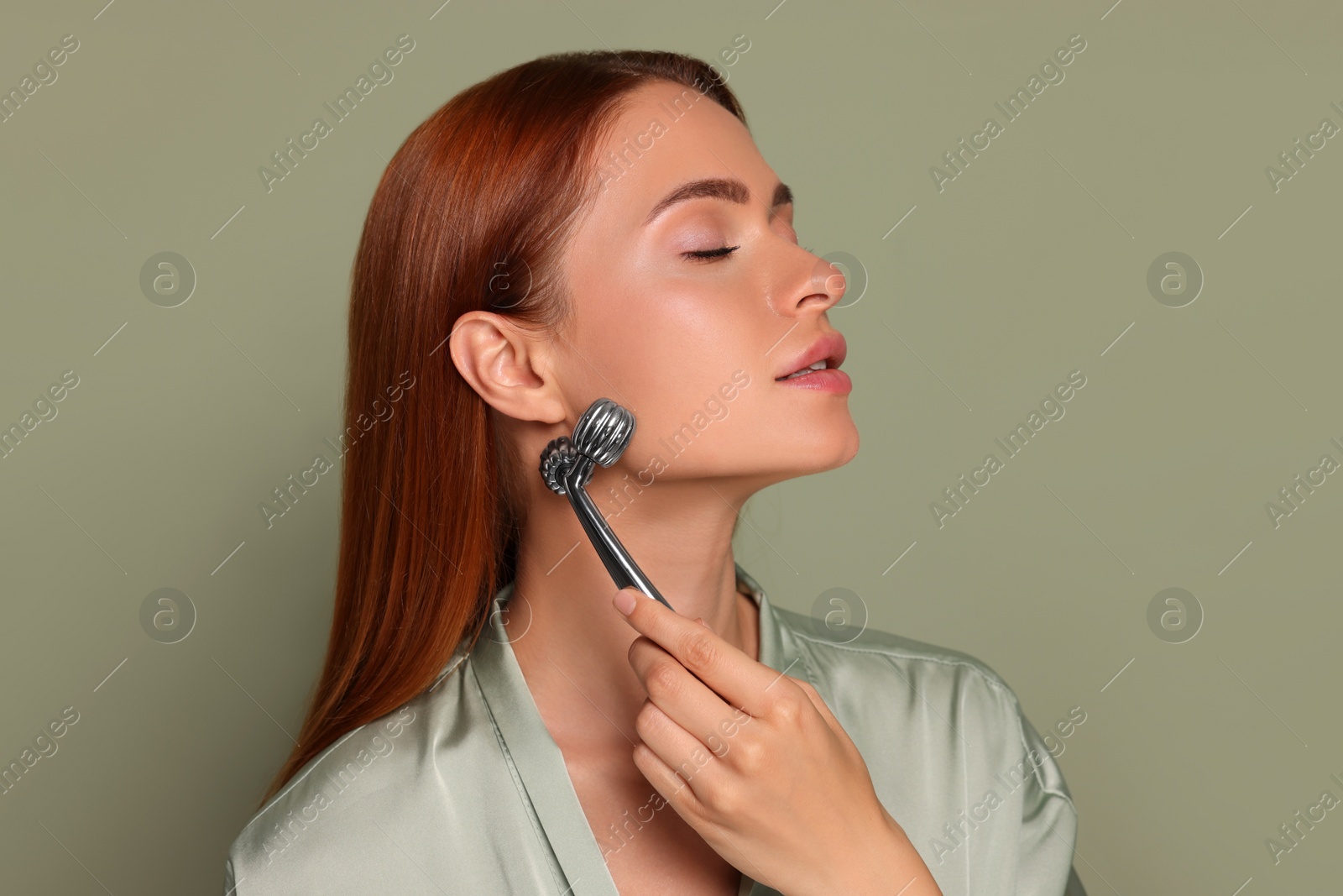 Photo of Young woman massaging her face with metal roller on green background