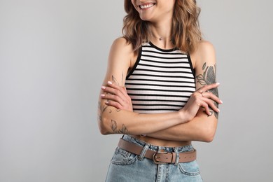 Photo of Beautiful woman with tattoos on body against grey background, closeup