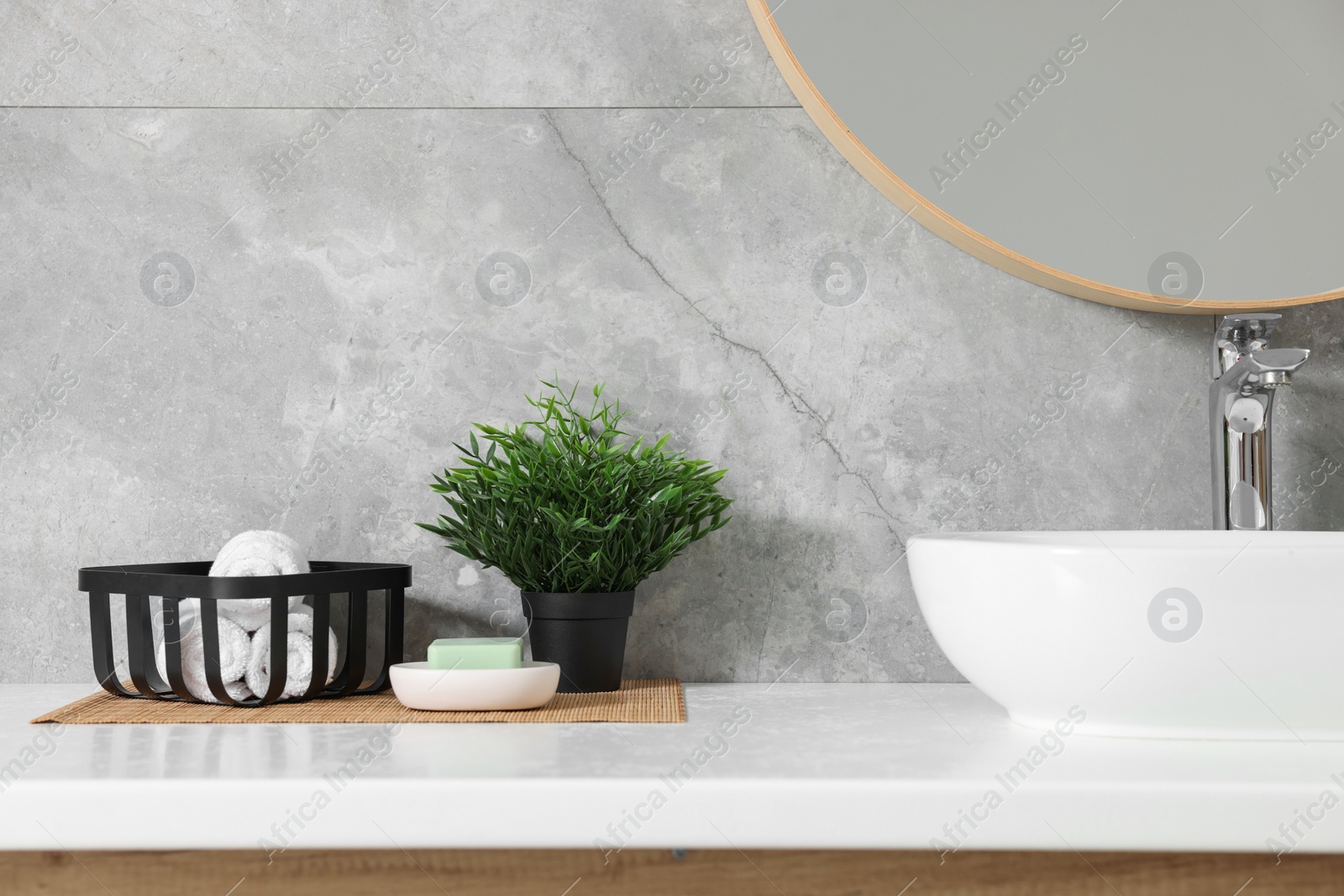 Photo of Potted artificial plants, rolled towels and soap near sink on bathroom vanity