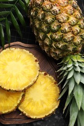 Photo of Slices of tasty ripe pineapple and whole fruit on black table, flat lay