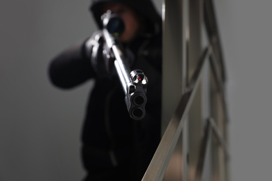 Photo of Hired professional killer indoors, focus on sniper rifle. Space for text