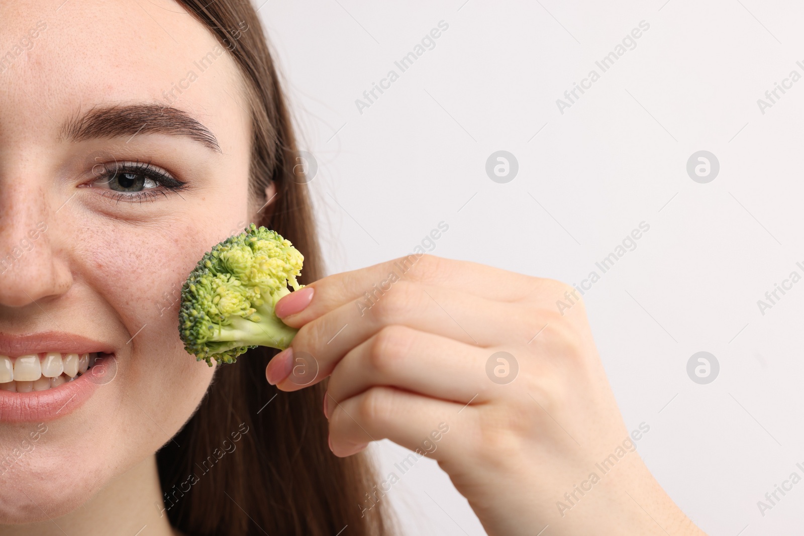 Photo of Smiling woman making fake freckles with broccoli and cosmetic product on light background, closeup. Space for text