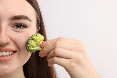 Smiling woman making fake freckles with broccoli and cosmetic product on light background, closeup. Space for text