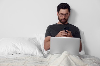 Photo of Handsome man using smartphone and laptop in bed, space for text