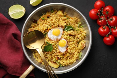 Photo of Tasty rice with meat, eggs and vegetables in frying pan near products on black textured table, flat lay