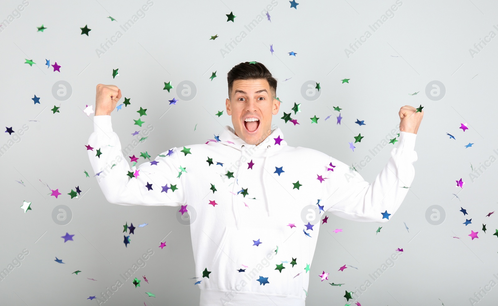 Photo of Emotional man and falling confetti on light grey background