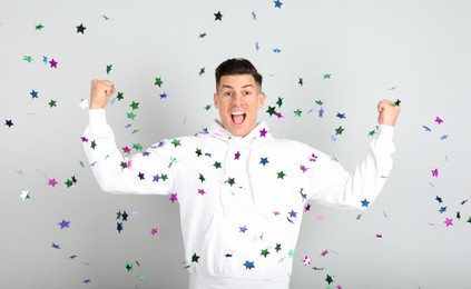 Emotional man and falling confetti on light grey background