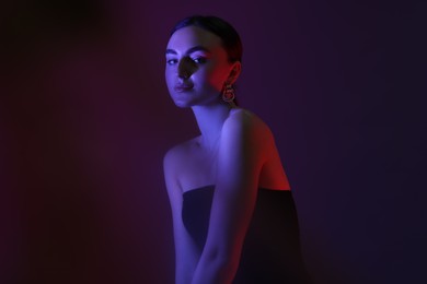 Portrait of beautiful young woman on color background in neon lights