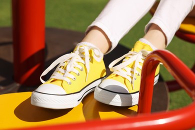 Photo of Woman in yellow classic old school sneakers on carousel outdoors, closeup